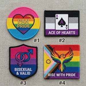 May include: Four embroidered patches with LGBTQ+ pride themes. The patches include a heart with "PAN PRIDE", an Ace of Hearts card, a shield with bisexual symbols and text, and a phoenix with "RISE WITH PRIDE".