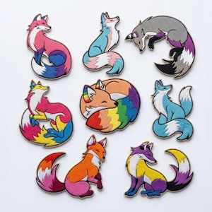 Könnte beinhalten: Eine Sammlung von neun gestickten Fuchsflicken in verschiedenen Posen. Jeder Fuchs hat ein einzigartiges Farbschema, darunter Rosa, Blau, Orange und Lila, mit Regenbogen- und Flaggen-inspirierten Designs. Die Flicken befinden sich auf weißem Hintergrund.