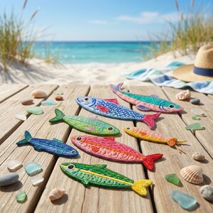 Puede incluir: Una colección de seis parches bordados con forma de pez en varios colores, incluyendo azul, verde, rosa y amarillo, con costuras detalladas y formas de aletas distintas, dispuestos sobre una superficie de madera con conchas y vidrio marino.