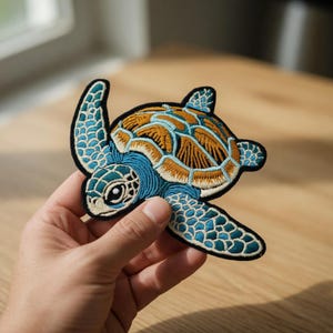 Puede incluir: Parche bordado de tortuga marina con un diseño detallado. La tortuga presenta un cuerpo azul, un caparazón marrón y un borde negro. Este parche decorativo se puede planchar o coser en ropa, bolsos u otros artículos de tela.