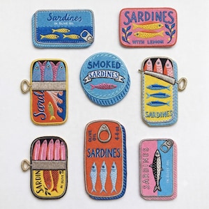 Può includere: Una collezione di toppe ricamate raffiguranti scatole di sardine. Le toppe presentano vari disegni, tra cui testi come "Sardines in Olive Oil" e "Smoked Sardines". La tavolozza dei colori comprende blu, rosa, arancione e giallo, con cuciture dettagliate.