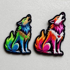 May include: Two embroidered patches featuring howling wolves. One wolf is in shades of green, blue, and gold. The other wolf is in shades of orange, pink, and purple, with a small red heart. Both patches have a black border.