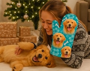 Puede incluir: Un guante de cocina turquesa con imágenes de golden retrievers, detalles de huesos blancos y estampados florales. El guante se sostiene cerca de un cachorro golden retriever. El fondo incluye un árbol de Navidad y regalos envueltos.