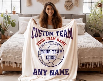 Puede incluir: Manta color crema con las palabras "CUSTOM TEAM" y "ANY NAME" en azul oscuro. La manta presenta un gráfico de balón de fútbol con espacio para el nombre y el logotipo del equipo. La manta es sostenida por una persona.