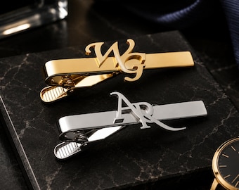 Puede incluir: Dos pisacorbatas de metal, uno con acabado en oro pulido con las letras WG y otro con acabado en plata pulida con las letras AR. Ambos clips tienen un diseño de barra rectangular lisa con un mecanismo de resorte para sujetar la tela.