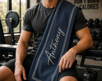 Puede incluir: Toalla de gimnasio personalizada azul marino con el nombre "Anthony" en escritura elegante. La toalla tiene un borde blanco y está sobre el hombro de una persona en un gimnasio. El texto "Excuses Don't Burn Calories" es visible en el fondo.