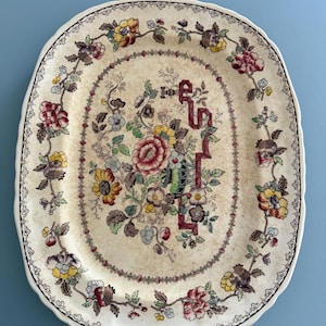 Puede incluir: Plato ovalado antiguo para servir con fondo crema. Presenta un diseño floral en tonos rojos, amarillos y azules, con un borde decorativo. El borde tiene un borde festoneado y un ribete negro. Una pieza vintage para servir.