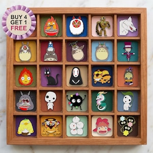 Puede incluir: Una bandeja de madera con veinticinco pines de esmalte que muestran varios personajes animados de las películas de Studio Ghibli, incluidos Totoro, Sin Cara y Calcifer. Una insignia circular morada en la esquina superior izquierda muestra el texto BUY 4 GET 1 FREE.