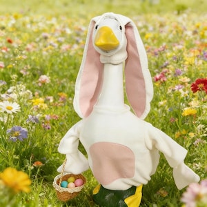 Puede incluir: Un ganso blanco con un disfraz de conejito, con orejas rosas y un parche rosa en el pecho. Sostiene una pequeña cesta llena de coloridos huevos de Pascua. El fondo es un campo de flores silvestres.