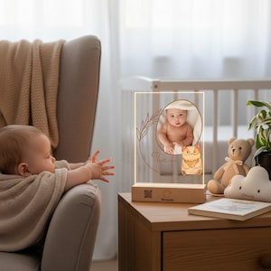 Può includere: Luce notturna con foto per bambini personalizzata con base in legno. Il pannello in acrilico trasparente presenta una foto del bambino all'interno di una ghirlanda floreale, il nome "Theo" e un piccolo gufo. Un bambino si protende verso la luce notturna.