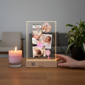 Può includere: Un'esposizione fotografica personalizzata per bambini con il nome "Samantha" e diverse foto di bambini. Il display è illuminato da una calda luce e poggia su una base di legno. Sono visibili anche una candela rosa e una pianta.