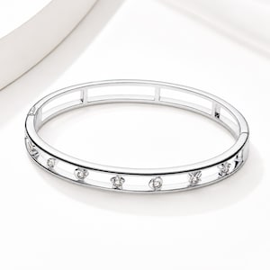 May include: A silver-toned hinged bangle bracelet featuring a double-band design with open space in the center. The outer band is accented with small, evenly spaced star-shaped cutouts, each containing a single clear, round-cut gemstone.