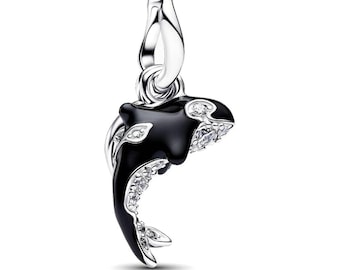 May include: A silver charm shaped like an orca whale, featuring a glossy black enamel body and clear sparkling stones embedded along the fins and tail. The charm includes a polished silver bail at the top for attachment to a bracelet or necklace.
