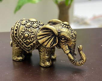 Könnte beinhalten: Detaillierte Messing-Elefantenfigur mit aufwendigen Mustern auf Rücken und Kopf. Der Elefant hat einen erhobenen Rüssel und steht auf einer dunklen Oberfläche. Die Figur ist ein dekoratives Objekt.