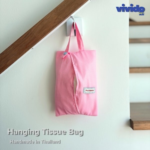 May include: A pink and white gingham fabric hanging tissue bag with a top handle, a light blue snap button closure, and a small rectangular white label with the text "Providential" stitched on the front, suspended from a white wall hook.