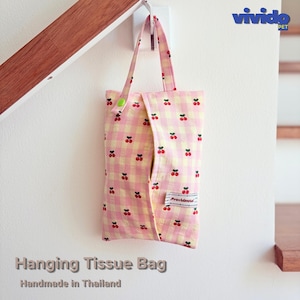 May include: A hanging tissue bag made of fabric with a light pink and yellow gingham pattern featuring small red cherry prints. The bag has a top handle with a green snap button closure and a small white rectangular label with the text Providential.