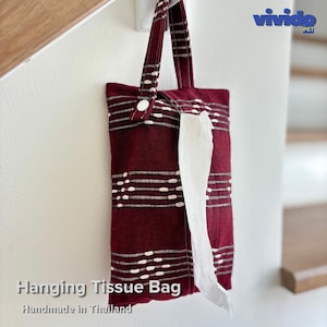 Puede incluir: Una bolsa de tela de color rojo oscuro para colgar pañuelos con rayas horizontales blancas tejidas y un solo botón de presión blanco en el asa. La bolsa muestra el texto "vivido PET" en la esquina superior derecha y "Hanging Tissue Bag Handmade in Thailand" debajo.