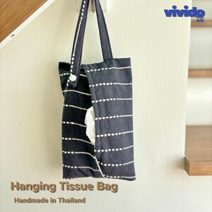 May include: A black hanging tissue bag featuring a white horizontal dashed pattern and a white snap button closure on the strap. The bag is made of fabric and contains white tissues. The text "vivido PET" appears in the top right corner.