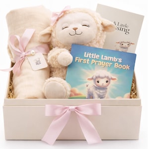 May include: A gift box with a plush lamb, a swaddling blanket, and two books. The lamb has a pink bow and closed eyes. The books are titled "Little Lamb's First Prayer Book" and "A Little Blessing". The box is tied with a pink ribbon.