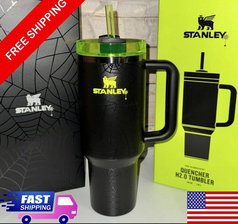 May include: Black Stanley Quencher H2.0 Tumbler with a green lid and straw. The tumbler has a handle and the Stanley logo in yellow. The packaging is visible in the background.