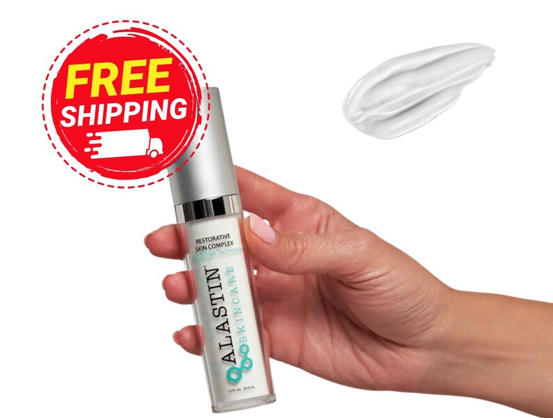 Puede incluir: Un frasco transparente de producto para el cuidado de la piel con tapa plateada se sostiene en una mano. El frasco tiene el texto "ALASTIN SKINCARE" y "Restorative Skin Complex". Una muestra de crema blanca est&aacute; al lado del frasco.