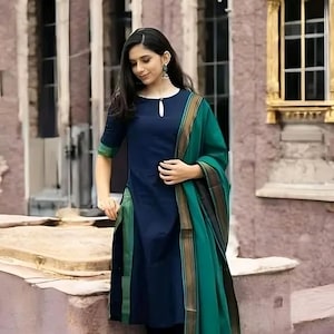 May include: A dark blue knee-length tunic with a small keyhole neckline and three-quarter sleeves, paired with black leggings and a long emerald green shawl featuring a dark brown and gold striped border along the edges of the fabric.