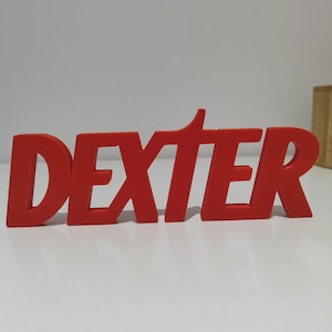 Può includere: Un'insegna rossa tridimensionale che riporta la parola DEXTER in un carattere grassetto senza grazie. La lettera T è stilizzata con un tratto verticale allungato verso l'alto e le lettere sono collegate per formare un oggetto unico e solido.