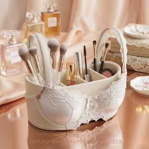 May include: A cream-colored bra-shaped organizer with a handle, filled with makeup brushes, lipsticks, and other beauty products. The organizer has white lace detailing and the text "LUXURY BRA-SHAPED ORGANIZER" at the bottom.