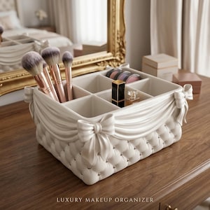 Puede incluir: Un organizador de maquillaje blanco acolchado con un diseño de tela drapeada y lazos. El organizador contiene brochas de maquillaje, lápiz labial y otros productos de belleza. El texto "LUXURY MAKEUP ORGANIZER" está en la parte inferior.