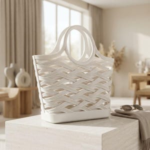 Puede incluir: Un bolso tote blanco con un dise&ntilde;o de celos&iacute;a trenzada y dos asas circulares integradas. El bolso tiene una base plana y s&oacute;lida con una estructura abierta, fabricado con un material liso y uniforme con un acabado blanco mate constante.
