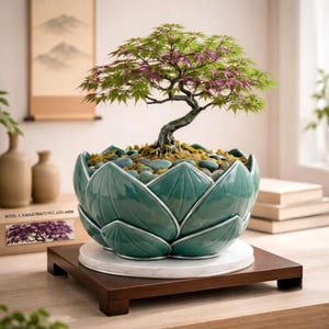 May include: A bonsai tree with green and purple leaves planted in a teal ceramic pot shaped like a lotus flower. The pot sits on a white circular base atop a square wooden stand. The soil is covered with smooth blue-grey river stones.