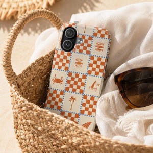 May include: A smartphone case featuring a checkered pattern in orange and cream, accented with small blue borders. The design includes various coastal icons such as a crab, a palm tree, a sailboat, fish, and a seashell printed on the cream squares.