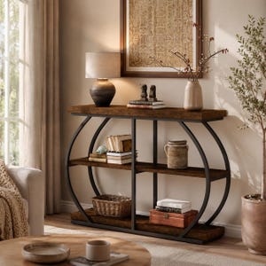 Peut inclure: Une console marron foncé avec une structure en métal noir et trois étagères. L'étagère supérieure présente une lampe, des livres et des objets décoratifs. Les étagères inférieures exposent des livres, un panier et une boîte en bois. Une œuvre d'art encadrée est suspendue au-dessus.