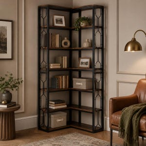 Op de afbeelding: Een hoge hoekboekenkast met een zwart metalen frame met geometrische zijpanelen en planken van donker hout. De kast is gevuld met diverse boeken, decoratieve vazen, ingelijste foto's en twee lichtgekleurde opbergdozen op de onderste planken.