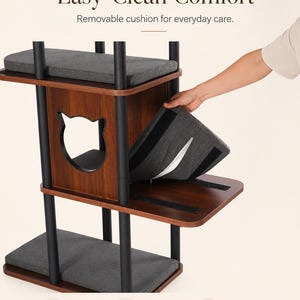 May include: A multi-level cat tree with dark wood-grain platforms and black metal supports. It features a cat-shaped cutout and removable gray fabric cushions with velcro attachments. Text on the image reads Easy-Clean Comfort, Lift, Clean, and Place Back.