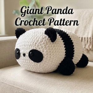 May include: A handmade, giant panda crochet pattern. The plush panda is white with black accents, including the ears, eyes, and a stripe down its back. The text "Giant Panda Crochet Pattern" is displayed on the image.