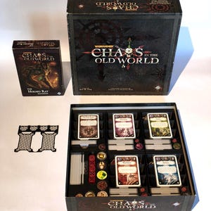 Op de afbeelding: Een Warhammer Chaos in the Old World bordspelset inclusief de hoofddoos, de The Horned Rat uitbreidingsdoos, een zwarte plastic inzetbak en een open speldoos met georganiseerde kaartspellen, rode dobbelstenen en diverse ronde fiches.