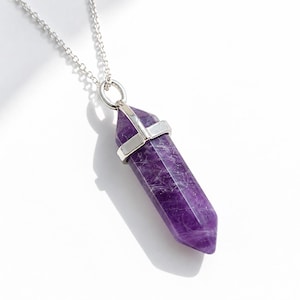 Könnte beinhalten: Eine Halskette mit einem facettierten, hexagonalen, tiefvioletten Amethyst-Kristallanhänger. Der Kristall ist in eine polierte, silberfarbene Metallfassung eingefasst und hängt an einer feinen, passenden silberfarbenen Gliederkette vor weißem Hintergrund.
