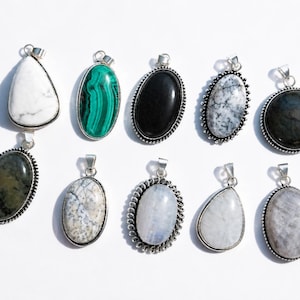 Peut inclure: Un ensemble de dix pendentifs en pierres précieuses sertis dans des montures en métal argenté. Les pendentifs présentent des formes variées, ovales et en goutte, avec des pierres aux tons blancs, verts, noirs, gris et bleus irisés aux motifs uniques.