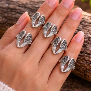 May include: Silver-toned rings with an open wing design. The rings are displayed on a hand, showcasing the intricate feather details. The rings are a jewelry item.