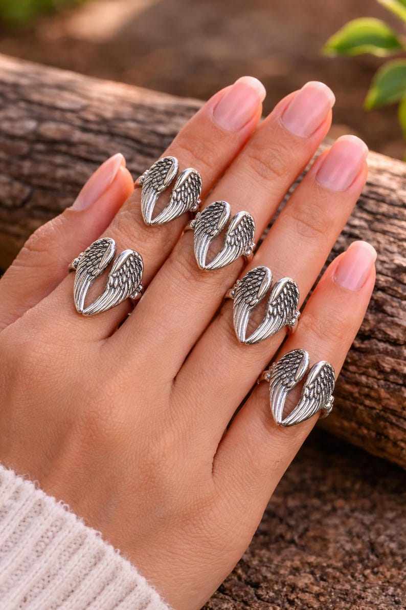 May include: Silver-toned rings with an open wing design. The rings are displayed on a hand, showcasing the intricate feather details. The rings are a jewelry item.