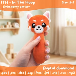 May include: An orange plush toy shaped like a red panda, held in a hand. The toy has white accents on its face and ears, with black eyes and a white muzzle. The text "ITH - In The Hoop Embroidery pattern" is visible. The size is 5x7.