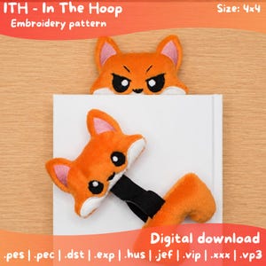 May include: An In The Hoop embroidery pattern digital download for a 4x4 size fox bookmark. The design features two plush orange fox heads with white accents and black elastic bands, one showing a neutral expression and one with an angry expression.
