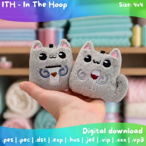 May include: Two small, grey, plush cat-shaped ornaments with embroidered details. One cat holds a white coffee cup with a brown heart, and the other holds a red wine glass. The text "ITH - In The Hoop", "Size: 4x4", and "Digital download" is visible.
