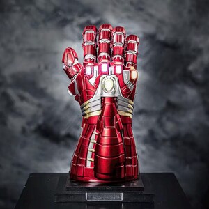 May include: A red and silver metallic gauntlet with a detailed design, featuring articulated fingers and glowing accents. The gauntlet is displayed on a black base, set against a dark, smoky background. A collectible item.