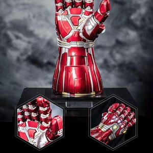 May include: A red and silver metallic gauntlet with articulated fingers, displayed on a black base. The gauntlet features intricate paneling and detailing, with a glossy finish. The image includes close-up views of the gauntlet's design and text in Chinese.