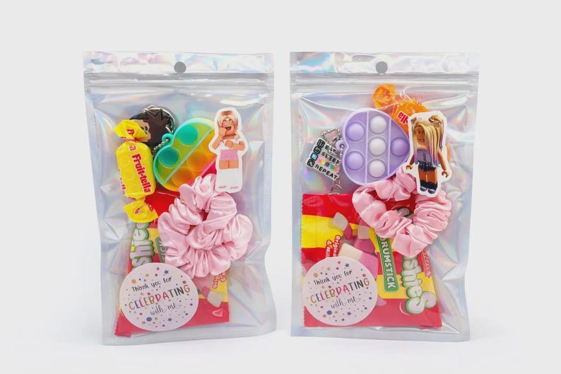 May include: Two iridescent plastic pouches containing party favor sets. Each bag includes a pink fabric scrunchie, a small fidget toy, a character sticker, and assorted candies. A circular sticker on the front of each bag reads Thank you for CELEBRATING with me.