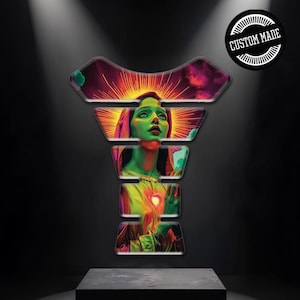 Può includere: Un proteggi-serbatoio per moto personalizzato con una vivace illustrazione di una donna con la pelle verde e un alone di luce. L'opera d'arte è ambientata su uno sfondo scuro, con le parole "CUSTOM MADE" in un design circolare.