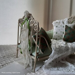May include: A white metal doll bed with a green and white striped mattress, a white lace blanket, and green and white pillows. The bed is decorated with white lace and green ribbon.