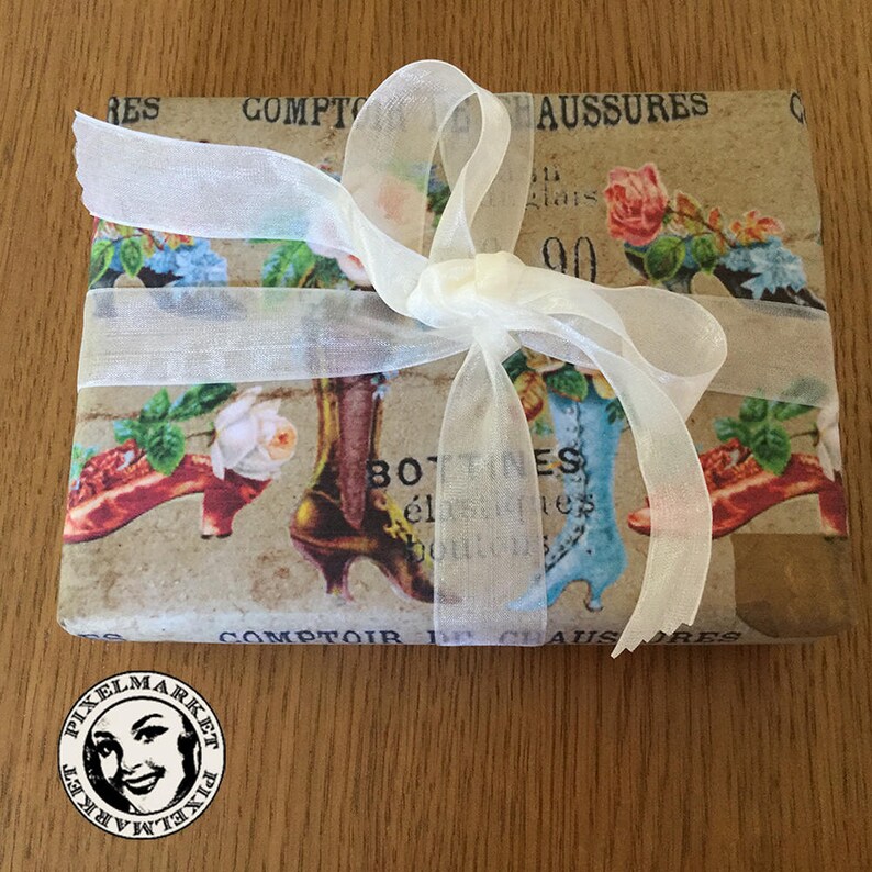 Op de afbeelding: Een bruine papieren cadeaudoos verpakt met een wit doorschijnend lint en gebonden met een strik. De doos is versierd met een vintage print van schoenen en bloemen. De tekst op de doos luidt "COMPTOIR DE CHAUSSURES".
